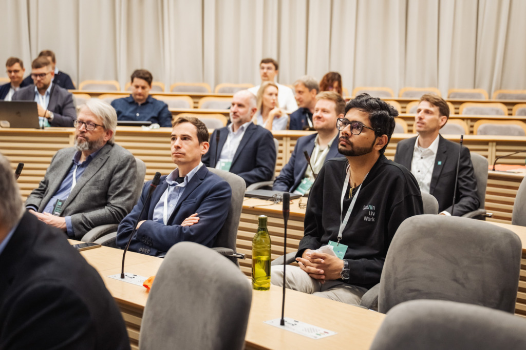 Participants at the SustAInLivWork Annual Summit 2026 listen to a presentation on data infrastructure and AI solutions. Attendees sit throughout the conference room while a speaker presents at the front.