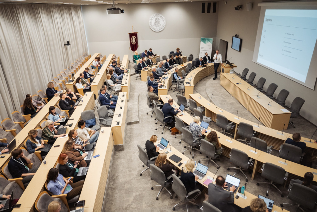 Participants at the SustAInLivWork Annual Summit 2026 listen to a presentation on data infrastructure and AI solutions. Attendees sit throughout the conference room while a speaker presents at the front.