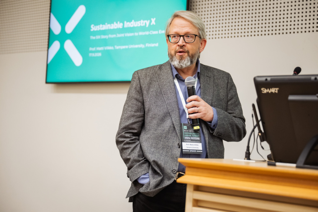 Prof. Matti Vilkko speaks into a microphone at the SustAInLivWork Annual Summit 2026 during a presentation